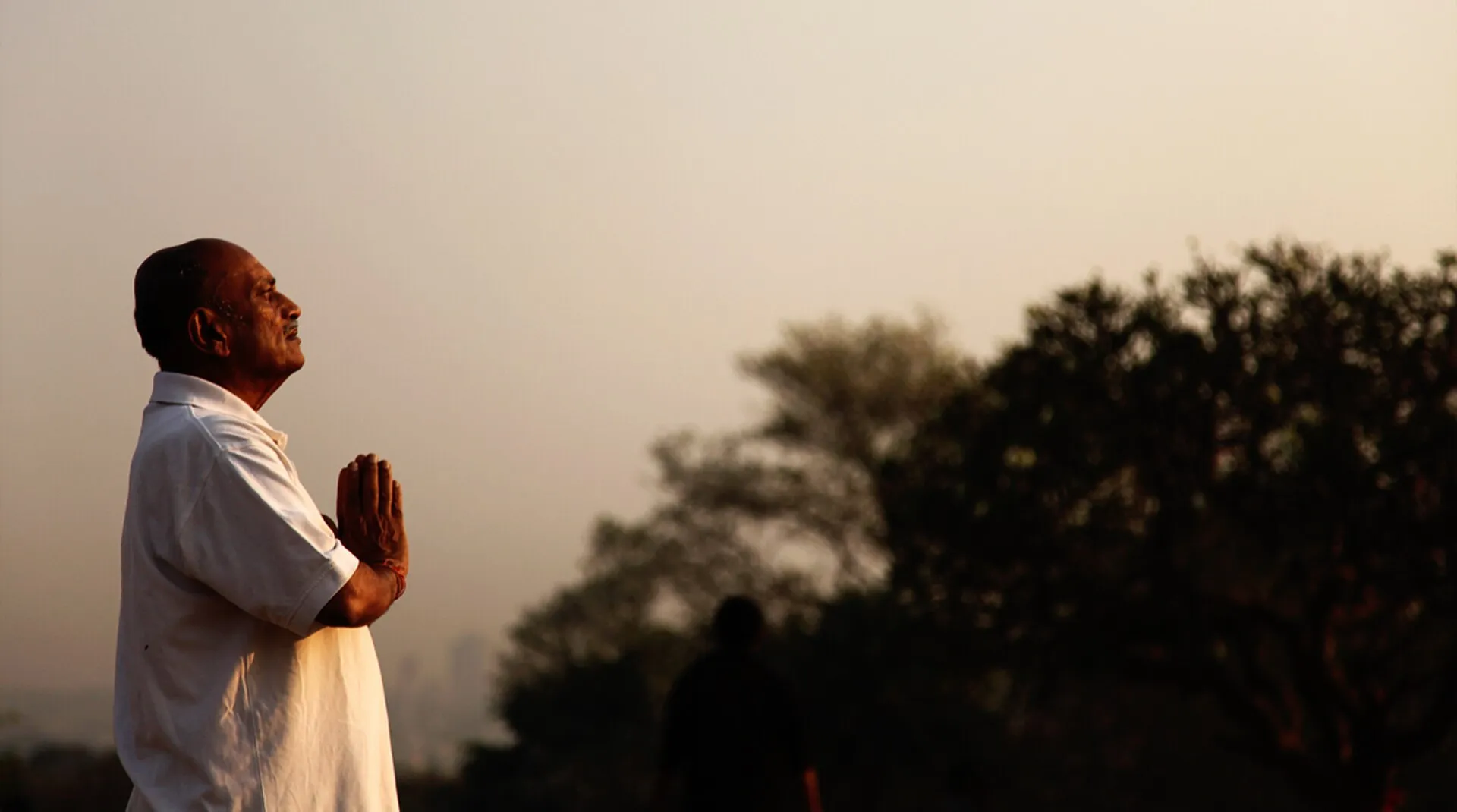 A person facing the sunrise with hands pressed together in quiet reflection
