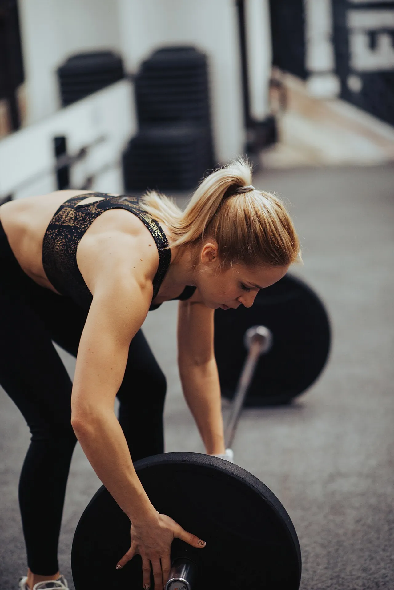 A woman mid-lift, gripping a loaded barbell in a gym
