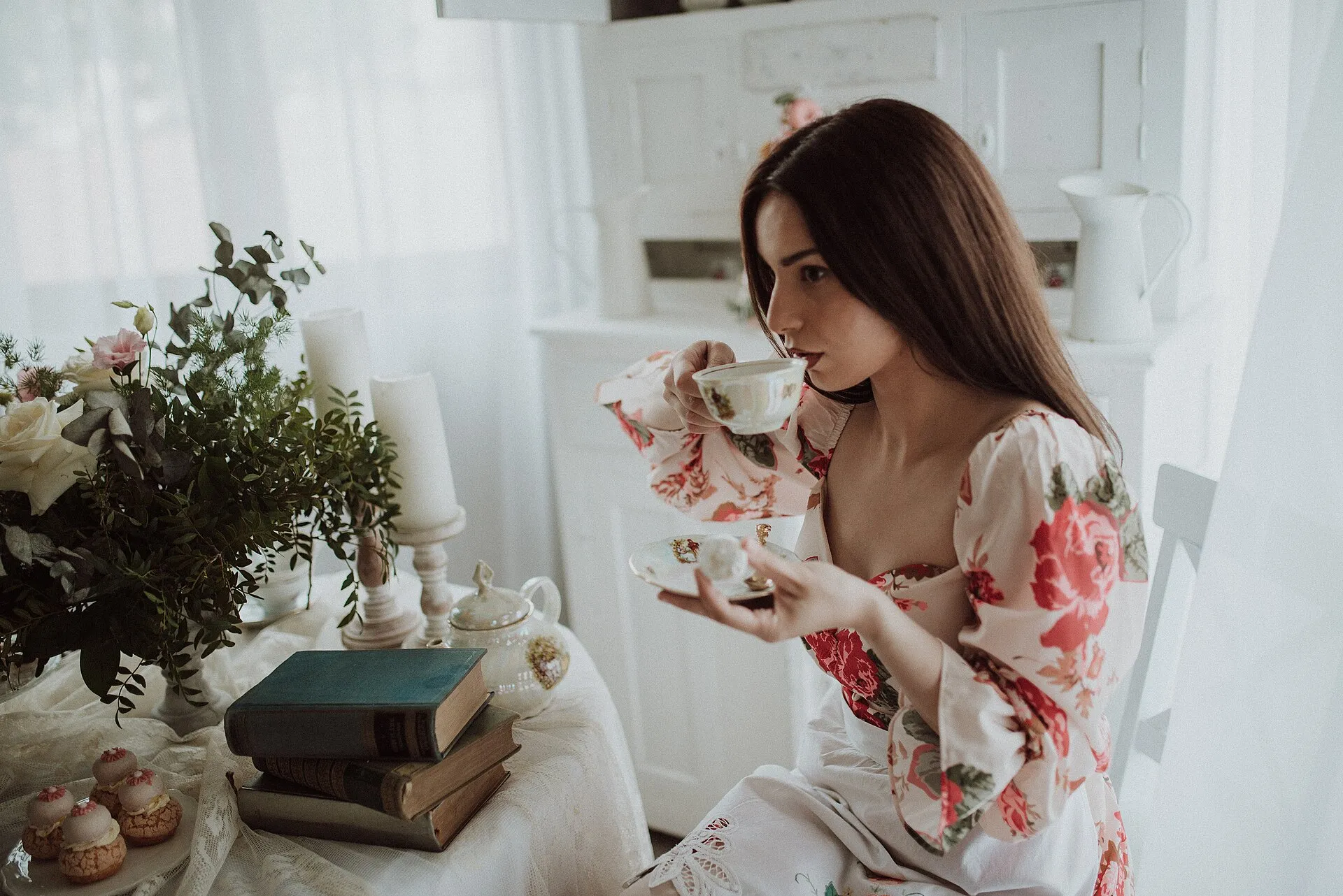 A woman drinking tea at a table set with flowers and books