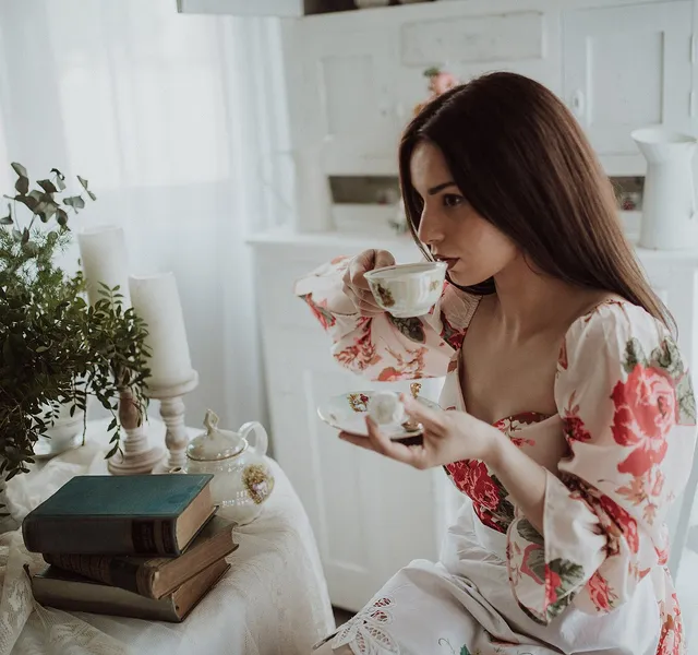 A woman drinking tea at a table set with flowers and books