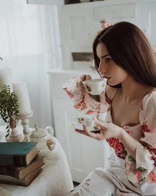 A woman drinking tea at a table set with flowers and books