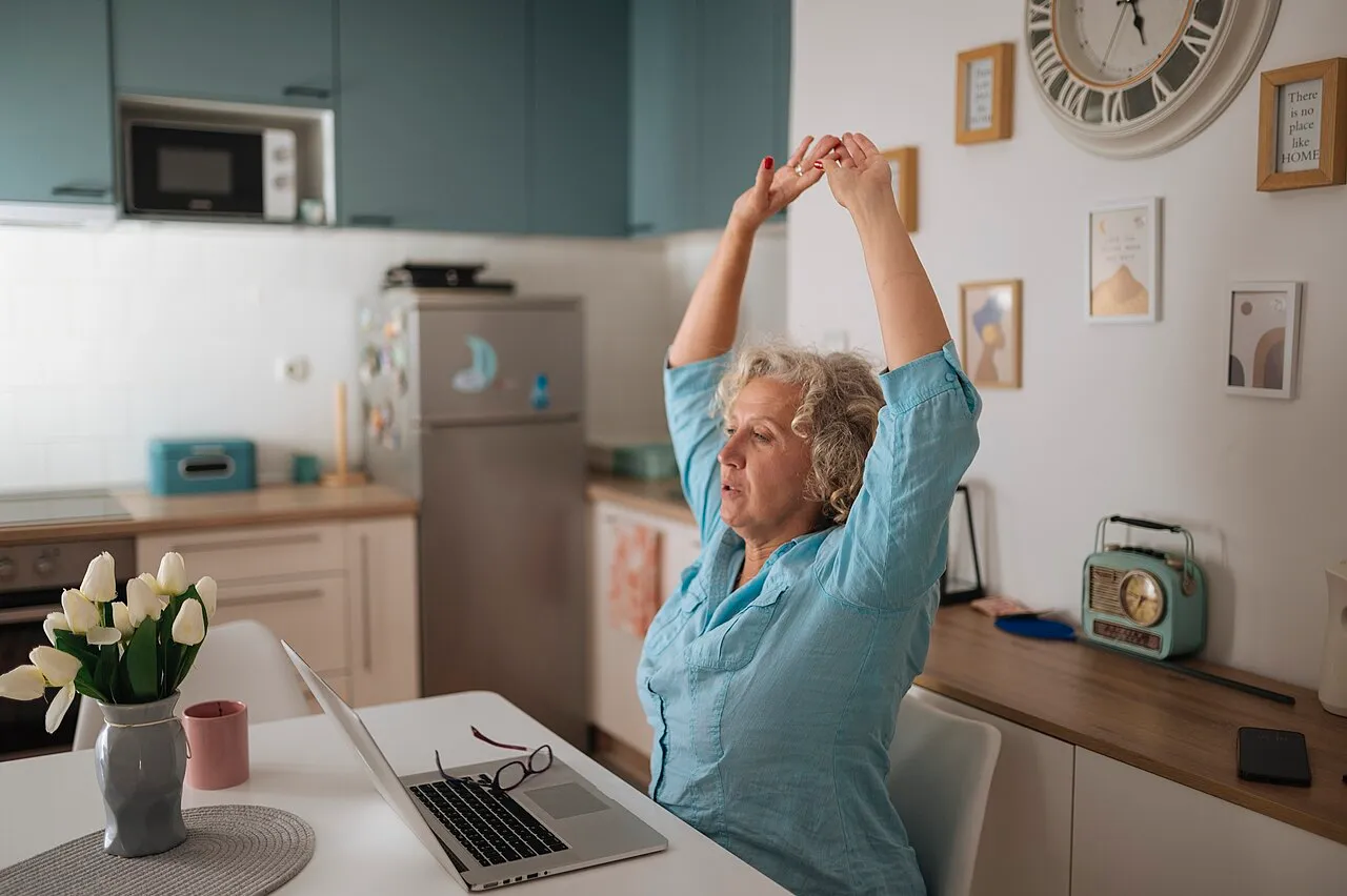 A woman stretching with her arms overhead at her desk during a work break