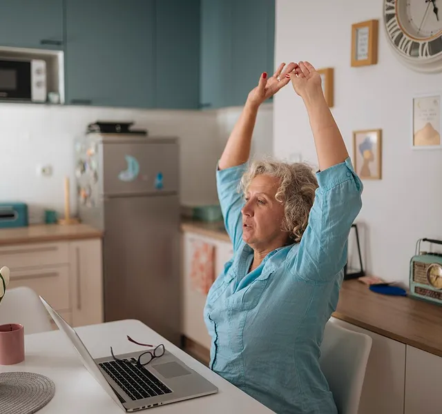 A woman stretching with her arms overhead at her desk during a work break
