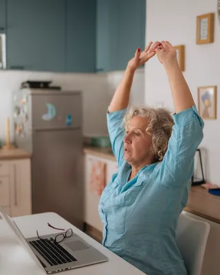 A woman stretching with her arms overhead at her desk during a work break