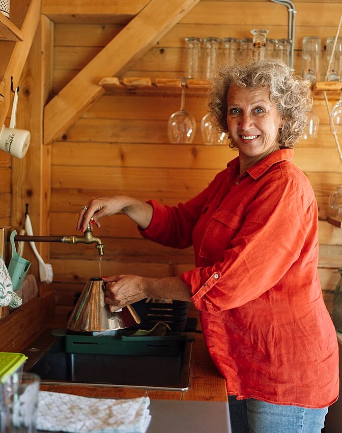 A woman smiling while preparing coffee in a cozy wooden kitchen