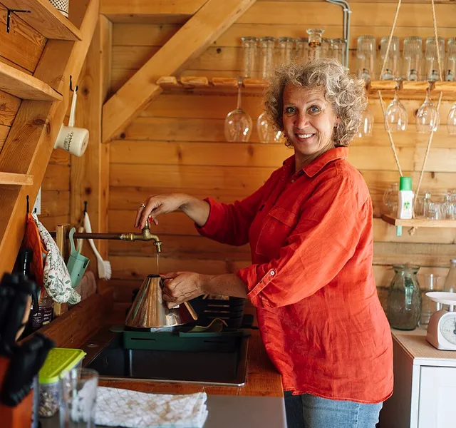 A woman smiling while preparing coffee in a cozy wooden kitchen