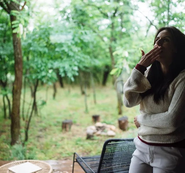 A woman standing on a porch breathing in fresh air surrounded by trees