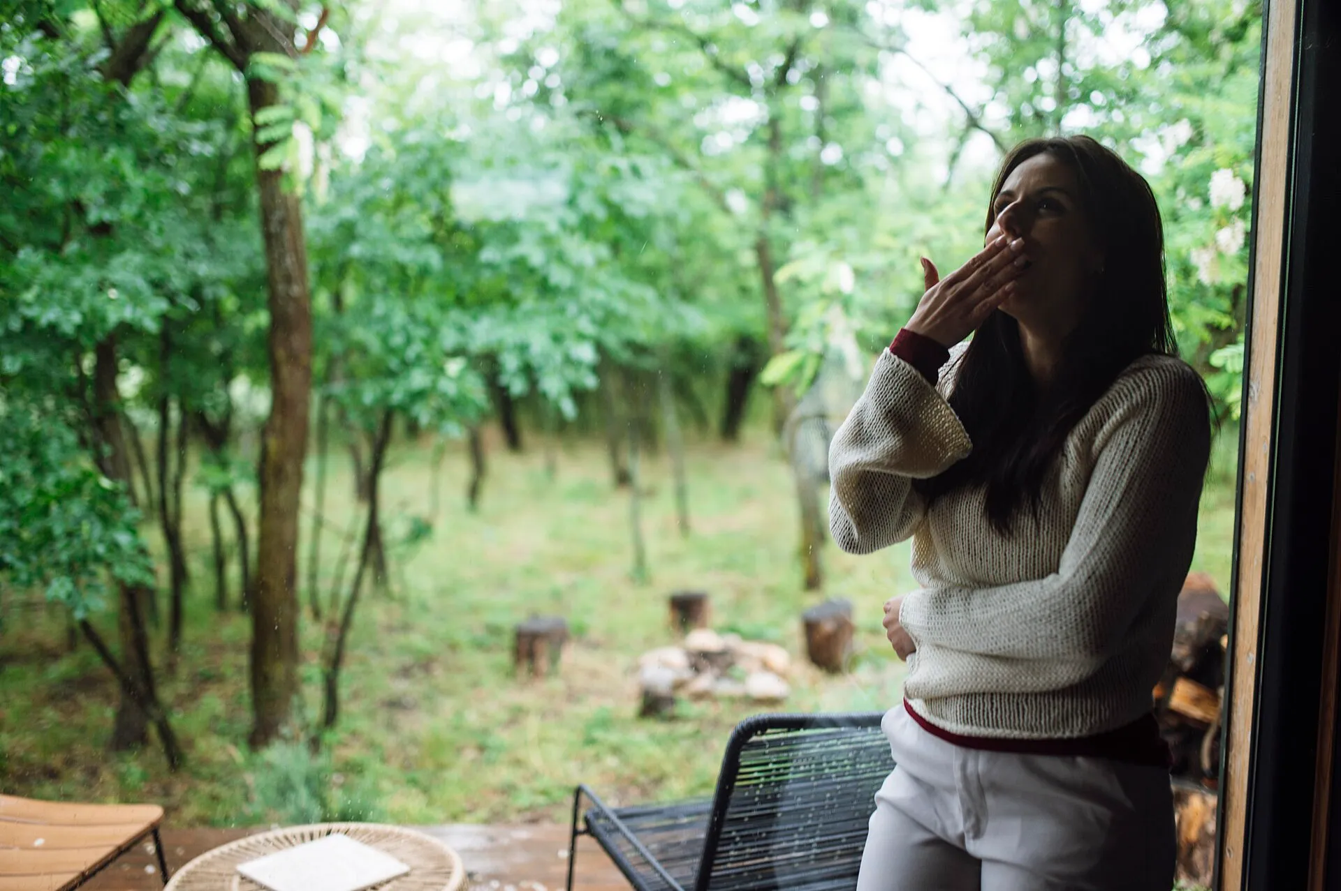 A woman standing on a porch breathing in fresh air surrounded by trees