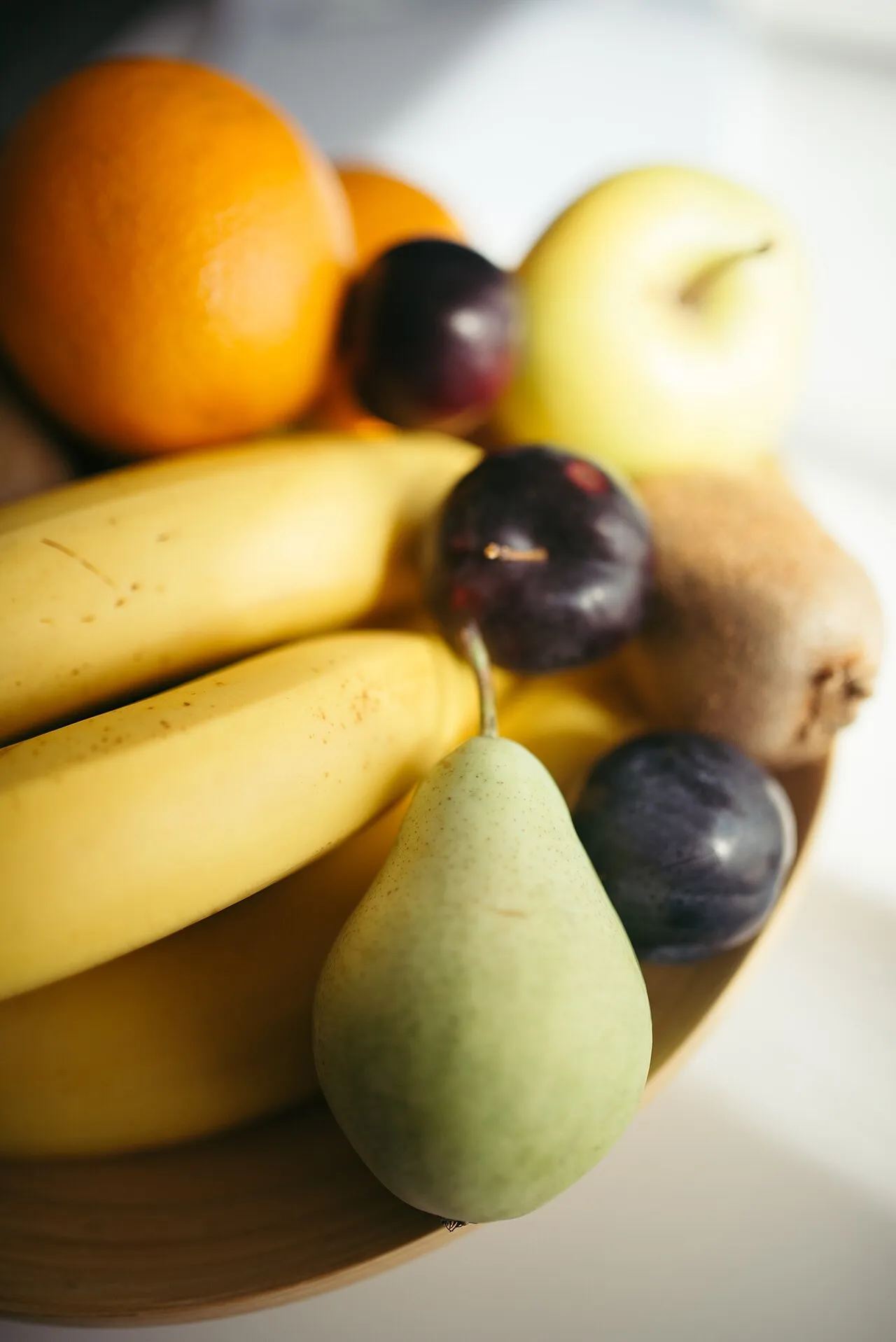 A wooden bowl piled with bananas, citrus, grapes, and a pear