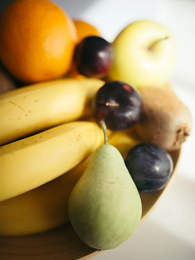 A wooden bowl piled with bananas, citrus, grapes, and a pear
