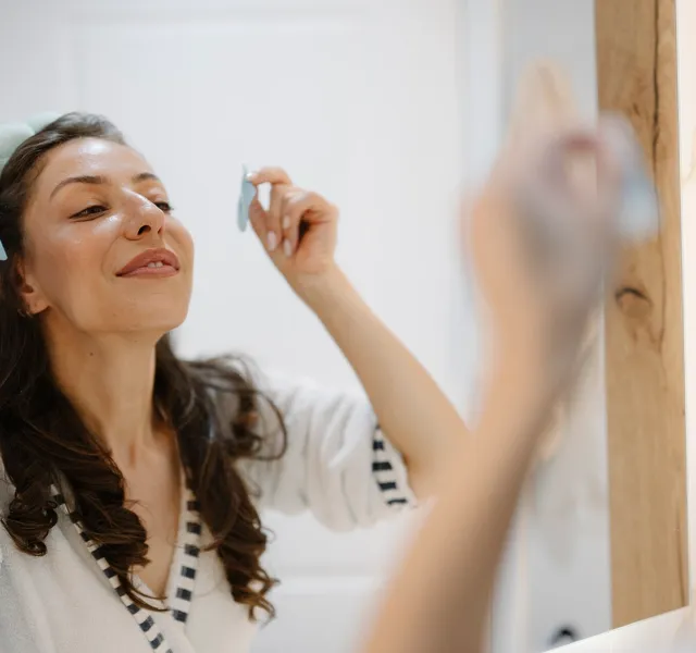 A woman uses a skincare tool while looking in a mirror