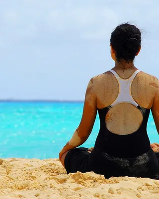 A woman seated in a meditation pose on the sand, facing turquoise water